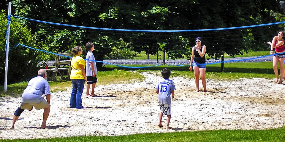 Families enjoying a game of sand volleyball at Elizabethtown / Hershey KOA Holiday during a camping vacation